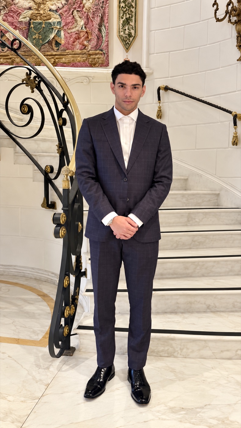 The founder of Vantic Agency, standing at the foot of a grand staircase in a dark suit